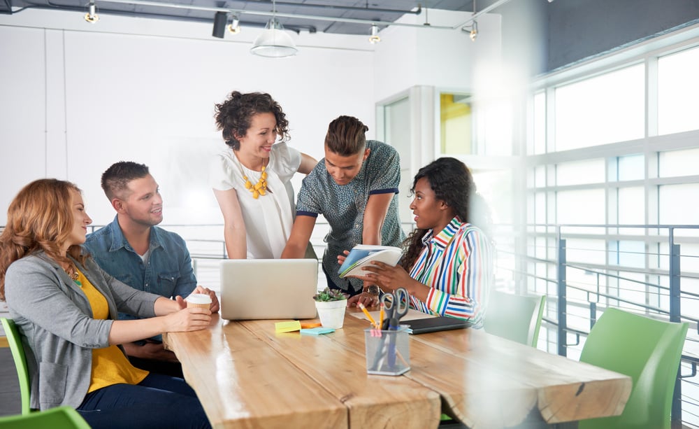 Multi ethnic group of succesful creative business people using a laptop during candid meeting